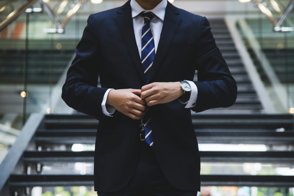 Confident man in a stylish suit standing tall, closing his jacket with a powerful demeanor, exuding self-assurance and professionalism.